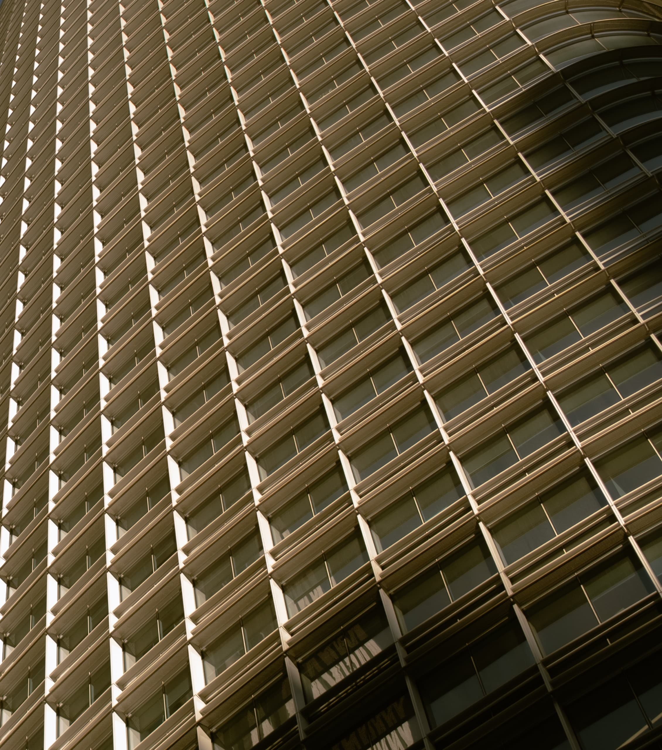 Tight low-angle of a curved skyscraper facade of horizontal sunshades in warm light.