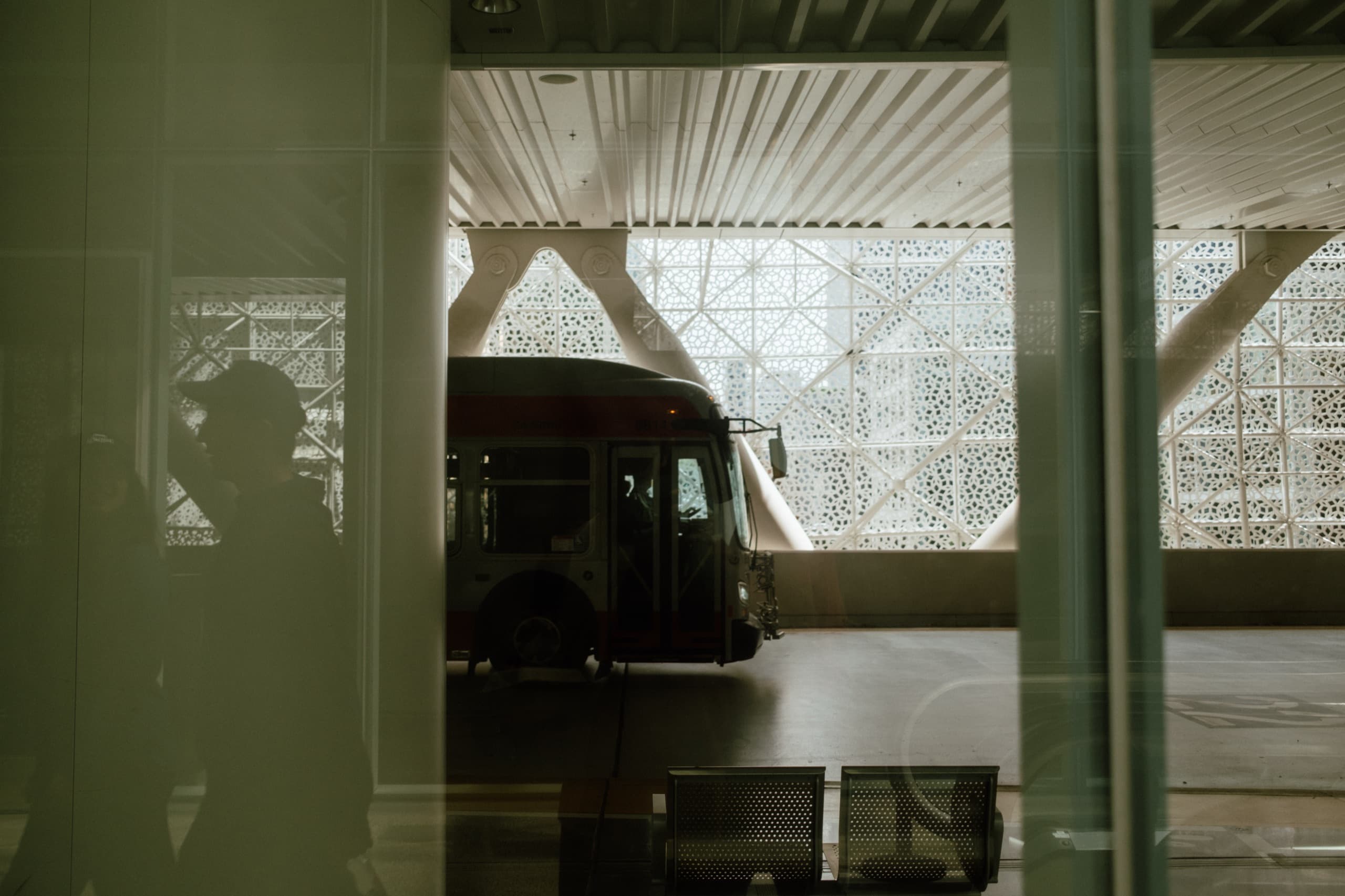Red-and-white bus at the transit center, seen through glass under the white lace facade.