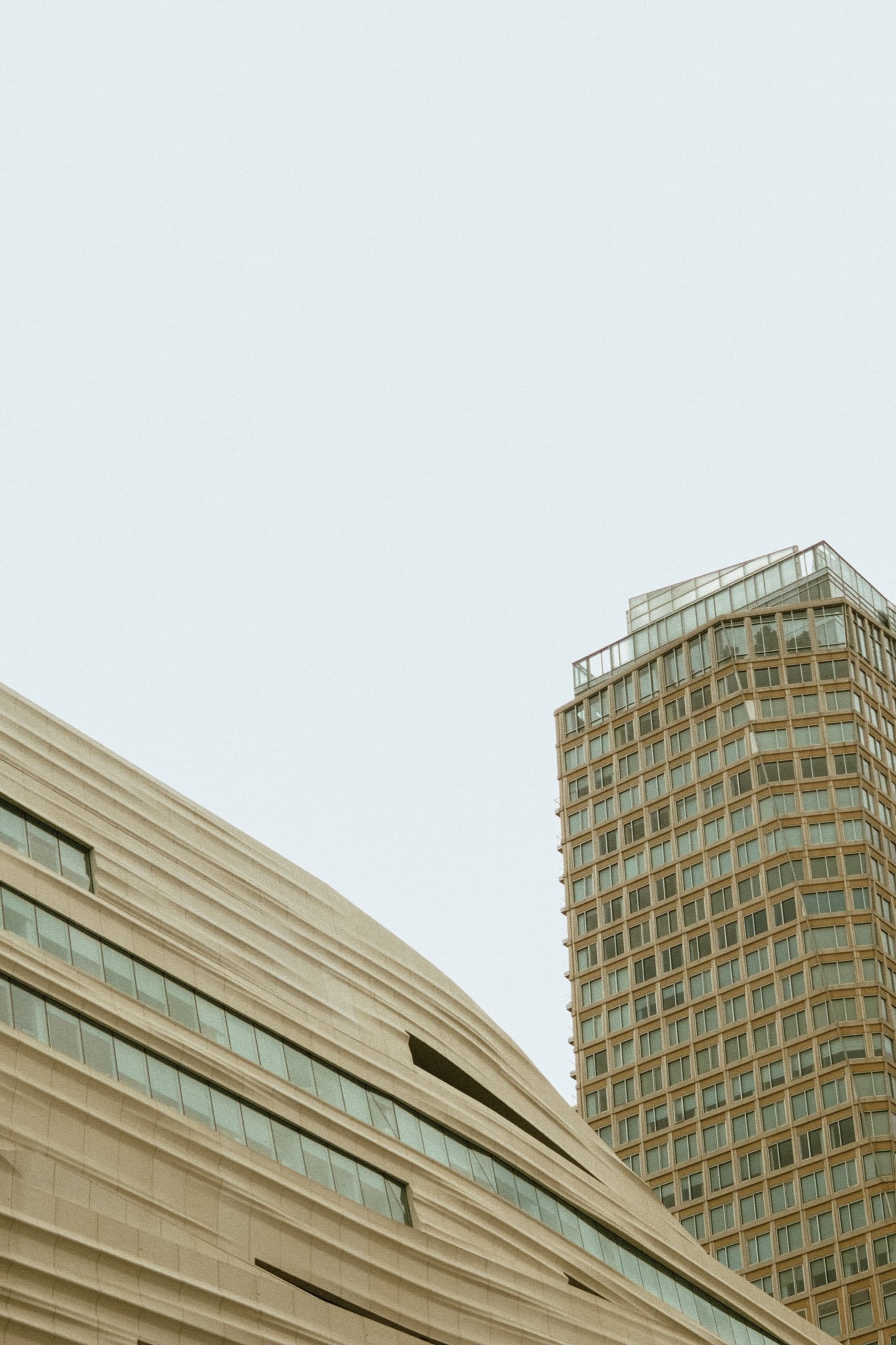 Wavy white perforated transit-center facade, brown faceted tower behind.