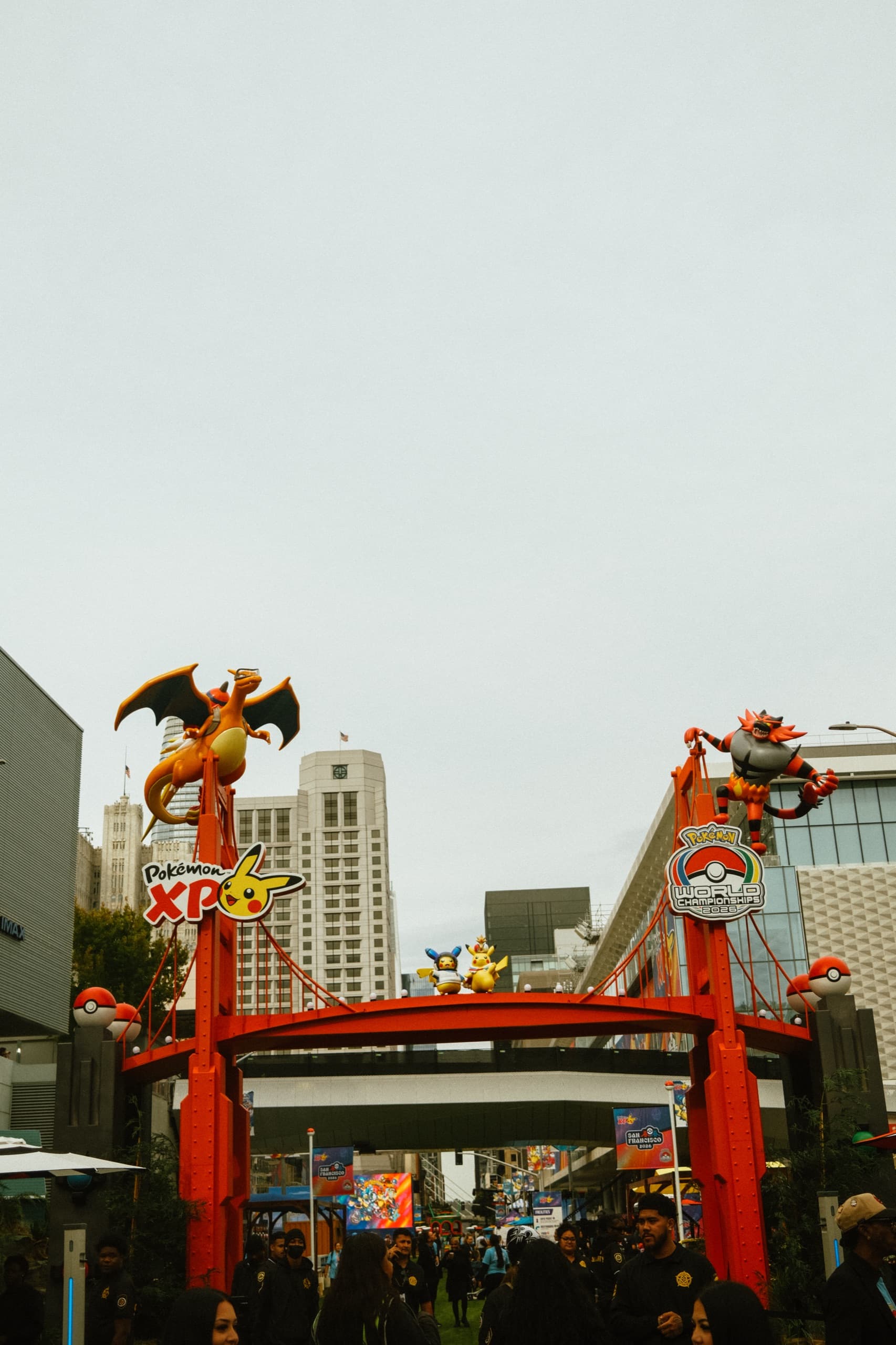 Red Golden Gate-style event gate with Charizard, Incineroar, Pikachu, crowd below.