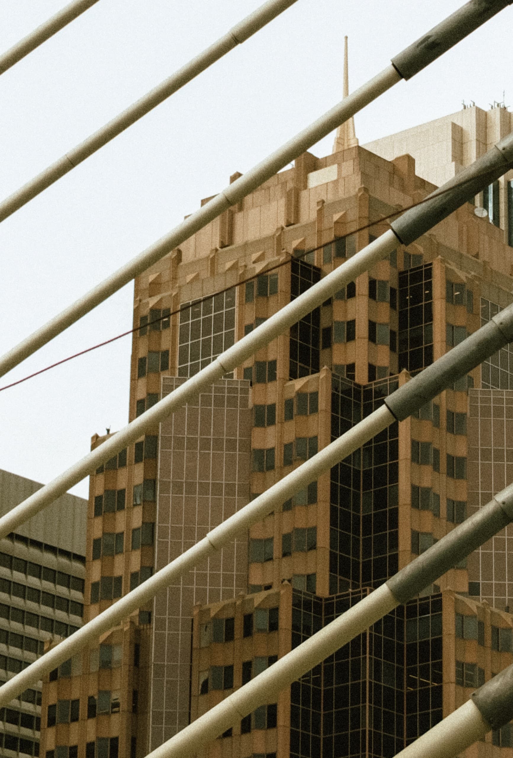 Tan stepped skyscraper with a spire, seen through diagonal bridge cables.